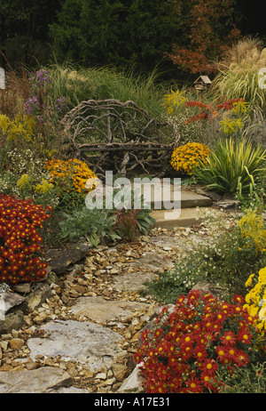 Rustic handmade grapevine built wooden bench in bright fall home flower garden with stone path in orange and yellow blooming flowers, Missouri, USA Stock Photo