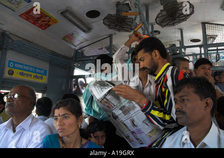 India Maharashtra Mumbai area suburb train crowd of people in the train with man reading newspaper standing and fans on ceiling Stock Photo