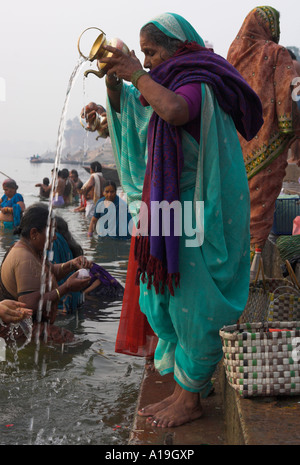 India Uttar Pradesh Ganges valley Varanassi Kedar ghat at sunrise woman standing on ghat s steps and pouring water in the river Stock Photo