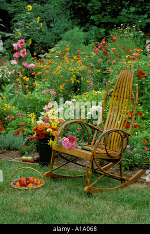 Unique bentwood Victorian rocking chair sits beside a colorful annual flower garden in s summer day with tomatoe harvest in basket, Missouri USA Stock Photo