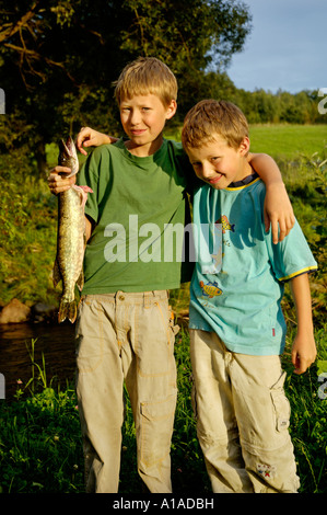 Boys, nine and eleven-year-old, are holding a fish pike they caught Stock Photo