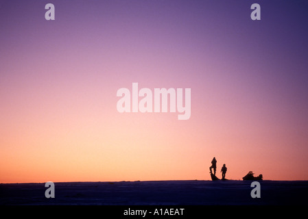 USA Alaska Nome Snowmobile rider and son wait for Iditarod mushers in hills near Bering Sea ice at dusk Stock Photo