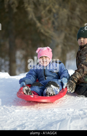 USA Alaska Anvik Young Athabascan Indian girl sleds down snow covered hill in rural village along Yukon River Stock Photo