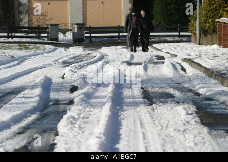 Tyre tire tracks in melting snow on tarmac road asphalt leading to two walkers in Glengormley Newtownabbey County Antrim Stock Photo