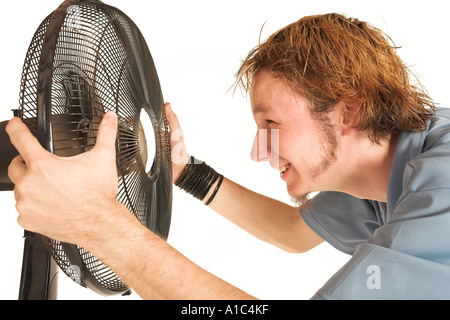 Man with blue shirt cooling down in front of a fan Stock Photo
