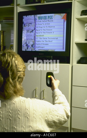 Woman uses Air Mouse remote control to scroll through movie selections on interactive television during Stock Photo