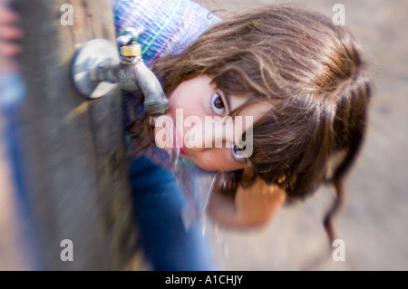 A young girl drinking from an outdoor faucet. Stock Photo