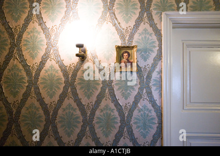 Bright lamp glowing next to a small framed baroque painting hung on a wall with floral pattern near the door Stock Photo