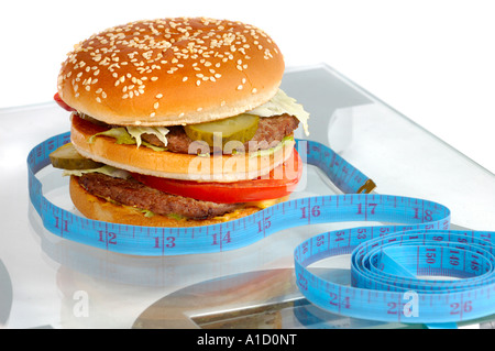 Hamburger and a measuring tape on bathroom scales Healthy Eating Dieting Healthcare Fitness Junk food concept Stock Photo