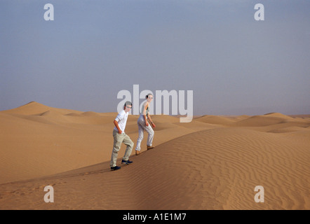 Young man and woman walk up sand dunes in the Sahara Desert Morocco Stock Photo
