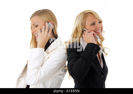 two young fair-haired woman standing back to back and telephoning Stock Photo