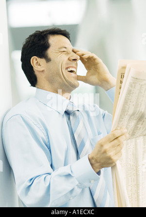 Businessman holding newspaper and laughing Stock Photo