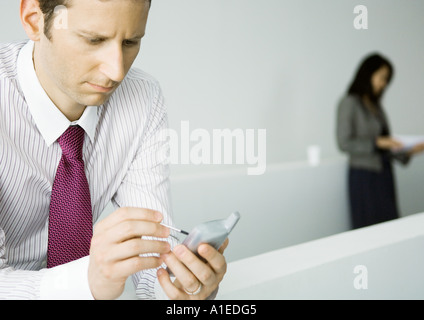Businessman using electronic organizer and furrowing brow, woman standing in background Stock Photo