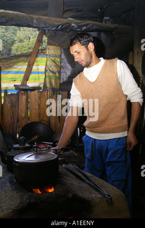 Indian local ethnic young man cooking in wooden shelter kitchen with pressure cooker on clay owen Stock Photo
