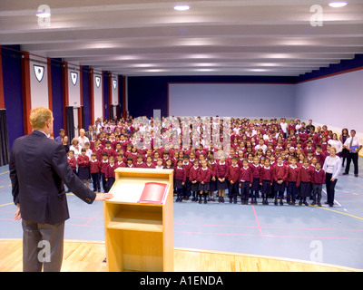 SCHOOL ASSEMBLY Head master teacher at lectern takes pupils and staff assembly in modern school hall Stock Photo