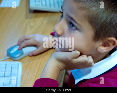 infant schoolboy with computer mouse and keyboard in uniform aged 3 to 5 years looking intently at kindergarten school computer screen in classroom Stock Photo