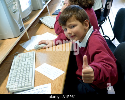 Confident junior schoolboy gives the thumbs up sign to camera in school computer classroom Stock Photo