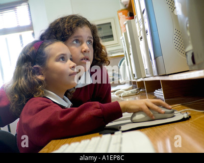 Two junior schoolgirls six to eight years work together on their computer terminal using a mouse to navigate in school computer classroom Stock Photo