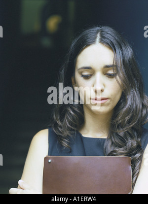 Woman holding folder in front of chest, looking down Stock Photo