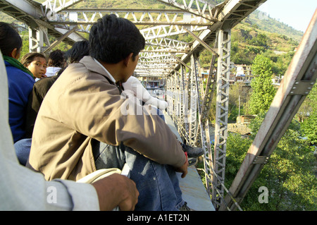 Passengers travelling on roof of overfull bus entering single track bridge, Kullu Valley in India Stock Photo