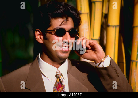 Indian man in a business suit wearing sunglasses and using a cellular phone outside Stock Photo