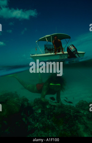 Over under view lady snorkeling on reef man on small outboard boat in Caribbean Stock Photo