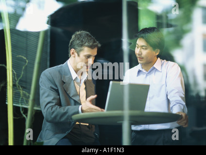 Businessmen sitting at cafe table, talking over laptop Stock Photo