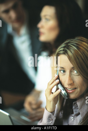 Businesswoman using cell phone in front of two co-workers Stock Photo
