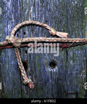 Plastic rope binding and rusty barbed wire on old farm gate post Stock Photo