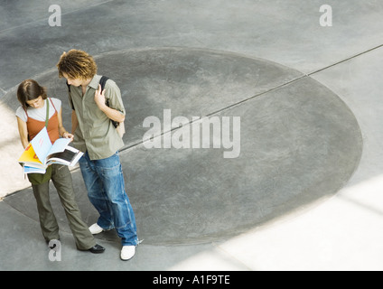 Two students standing in lobby looking at notebook together Stock Photo