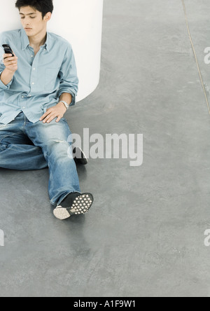 Young man sitting on floor looking at cell phone Stock Photo