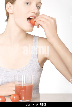 Young woman eating tomato, with glass of tomato juice Stock Photo