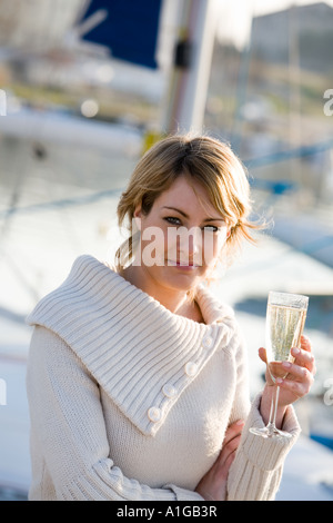 One beautiful young blond woman holding tall glass of bubbling champagne. Regattas in background. Daylight shot Stock Photo