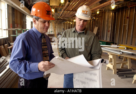 Architect and Construction foreman look over schematic drawings blueprints at construction site Stock Photo
