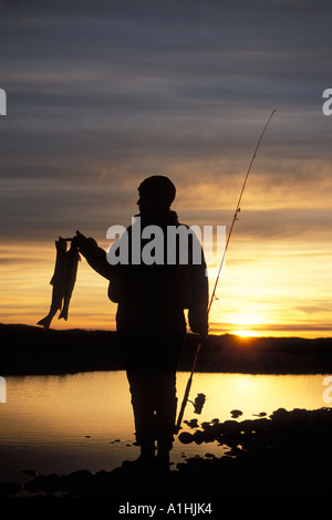 silhouette of a woman holding up catch of Arctic char Salvelinus alpinus along a river in the central Arctic North Slope Brooks Range Alaska Stock Photo