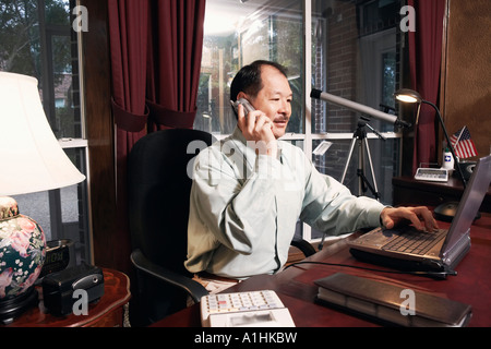 Senior man using a laptop talking on a cordless telephone Stock Photo