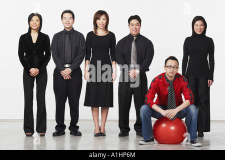 Portrait of a young man sitting on a ball with a group of business executives standing beside him Stock Photo