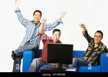 Close-up of three young men cheering in front of a flat screen monitor Stock Photo