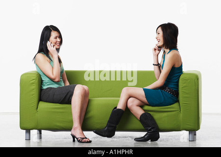 Side profile of two young women sitting on a couch talking on mobile phones