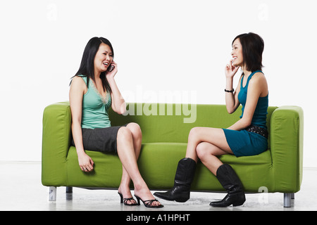 Side profile of two young women sitting on a couch talking on mobile phones