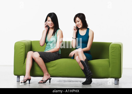 Two young women sitting on a couch talking on mobile phones