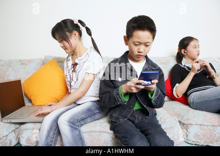 Boy sitting on a couch playing a video game beside his two sisters Stock Photo