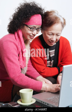Side profile of a mature woman sitting with her friend using a laptop Stock Photo