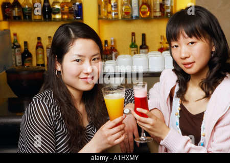 Portrait of two young women sitting at a bar counter raising a toast Stock Photo
