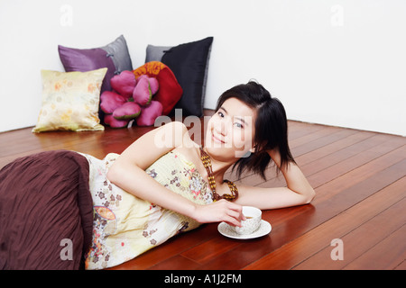 Portrait of a young woman lying on the floor and holding a cup of tea Stock Photo