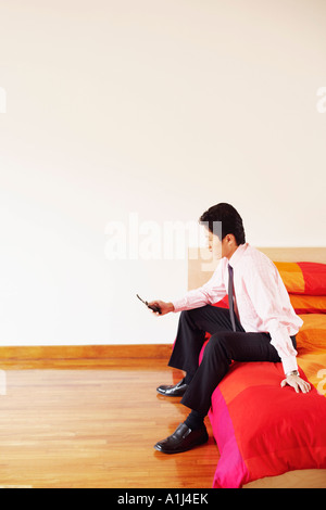 Side profile of a businessman sitting on the bed and operating a mobile phone Stock Photo