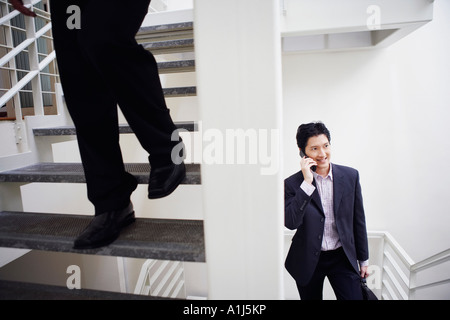 Low section view of a man walking down stairs with another businessman talking on a mobile phone