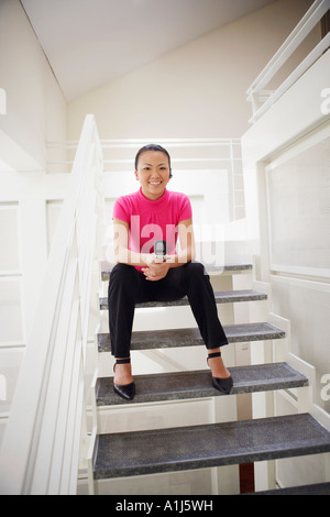 Portrait of a businesswoman sitting on a staircase and holding a mobile phone Stock Photo