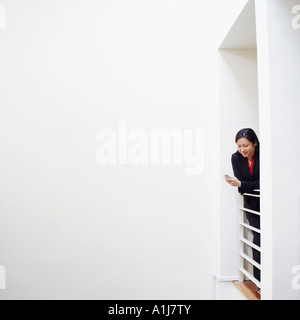 Businesswoman leaning over a railing and operating a mobile phone Stock Photo