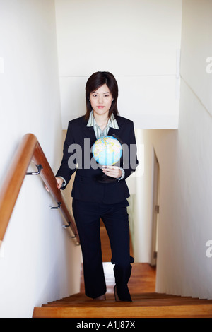 Portrait of a businesswoman holding a globe and walking on the staircase Stock Photo